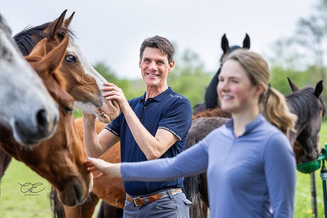 Das Bild zeigt einen Mann und eine Frau, die sich mit Pferden in einer Weide begeben haben.