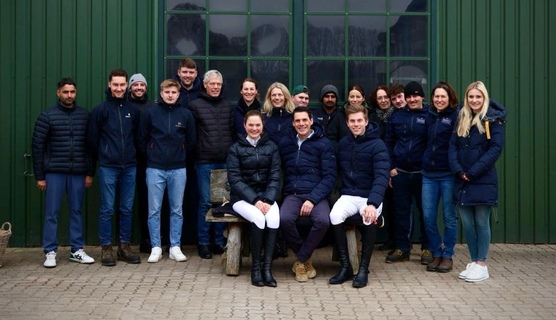 Das Bild zeigt eine Gruppe von 20 Menschen, die vor einem grünen Gebäude stehen, das wahrscheinlich ein Reiterhof ist.